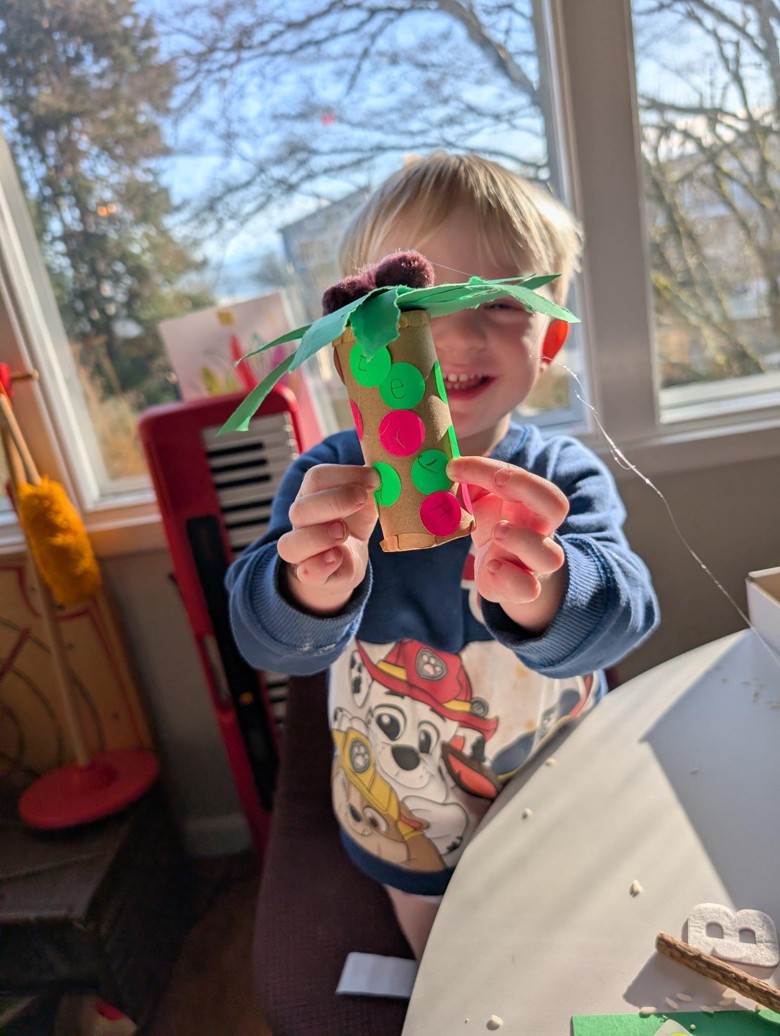 Young child proudly holding a handmade craft project from a Rooted in Writing subscription box activity, shared by a parent reviewer from Seattle, WA.